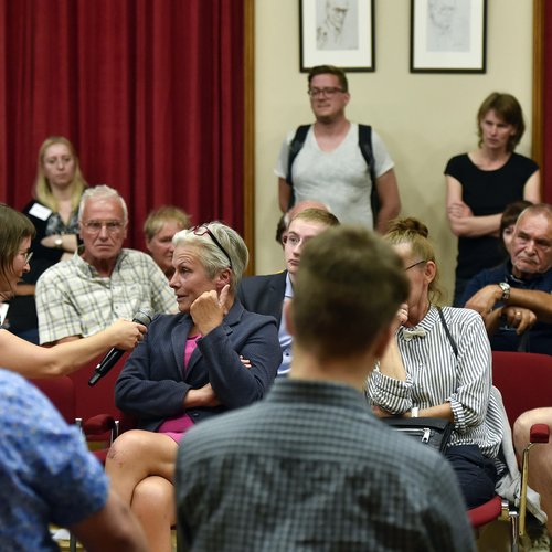 Menschen in Stuhlkreis diskutieren. Teilnehmerin aus dem Publikum erhält das Mikrofon